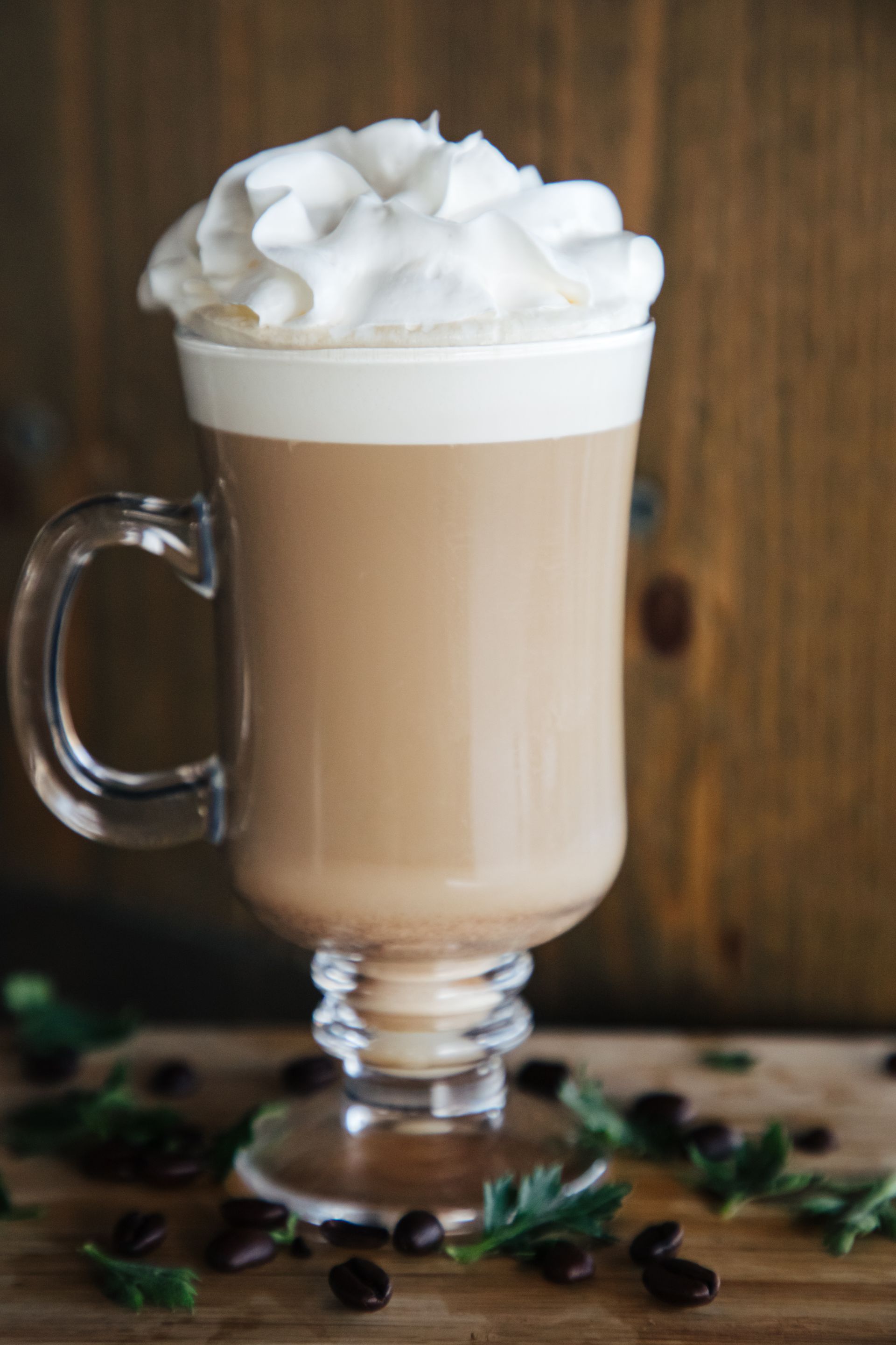 A glass of coffee with whipped cream on top is on a wooden table.