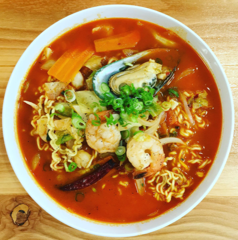 A bowl of soup with noodles and shrimp on a wooden table.