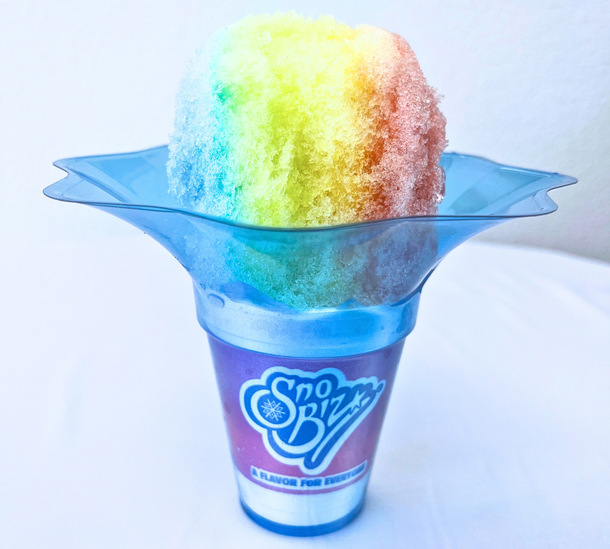 A rainbow colored shaved ice in a purple and blue cup