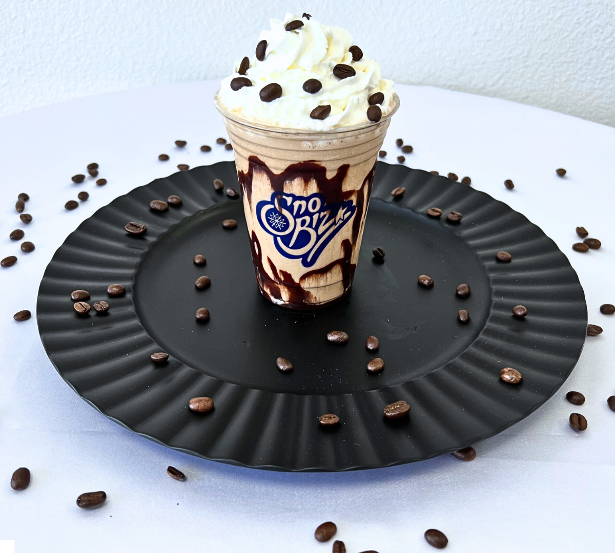 A cup of ice cream with whipped cream and chocolate sprinkles sits on a black plate