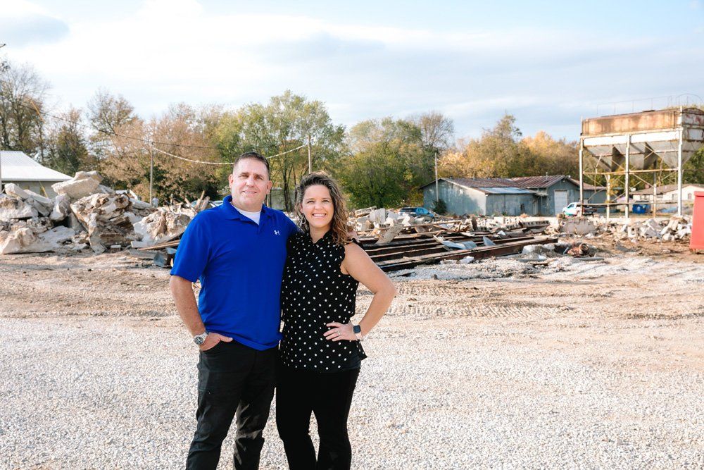 A man and a woman are standing next to each other in a gravel lot.