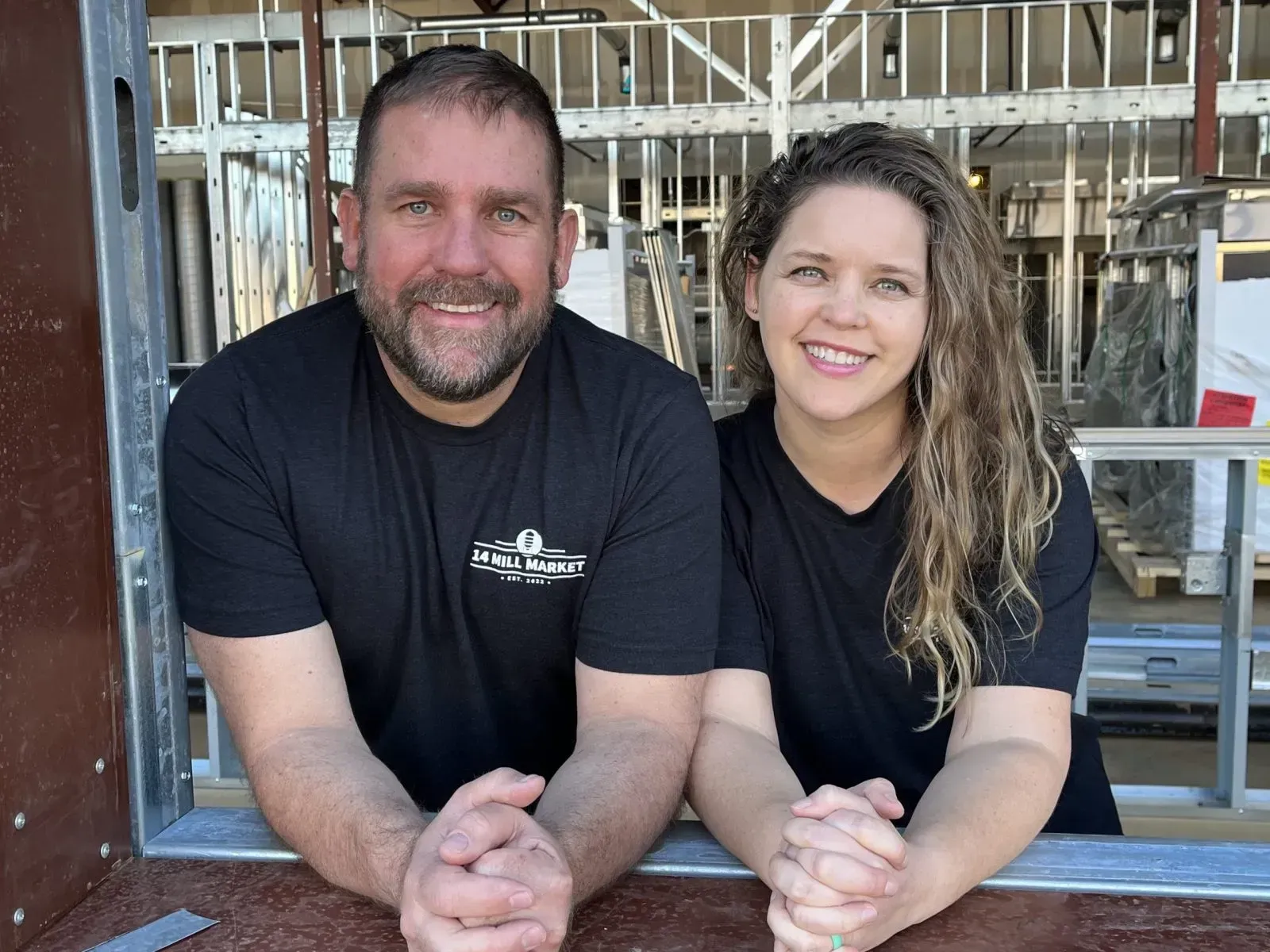 A man and a woman are posing for a picture in front of a building under construction.