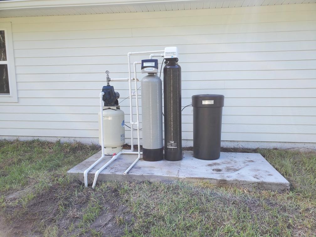 Water Tanks — Palatka, Fl — Moore’s Well Drilling Water filtration system on a concrete pad outside a house, consisting of tanks and pipes.
