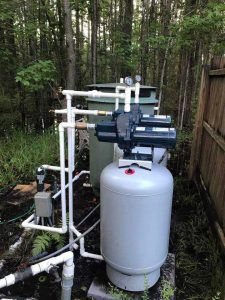 Water Pumps In The Yard — Palatka, Fl — Moore’s Well Drilling Well water system with pump, pressure tank, and pipes outdoors in a wooded area.