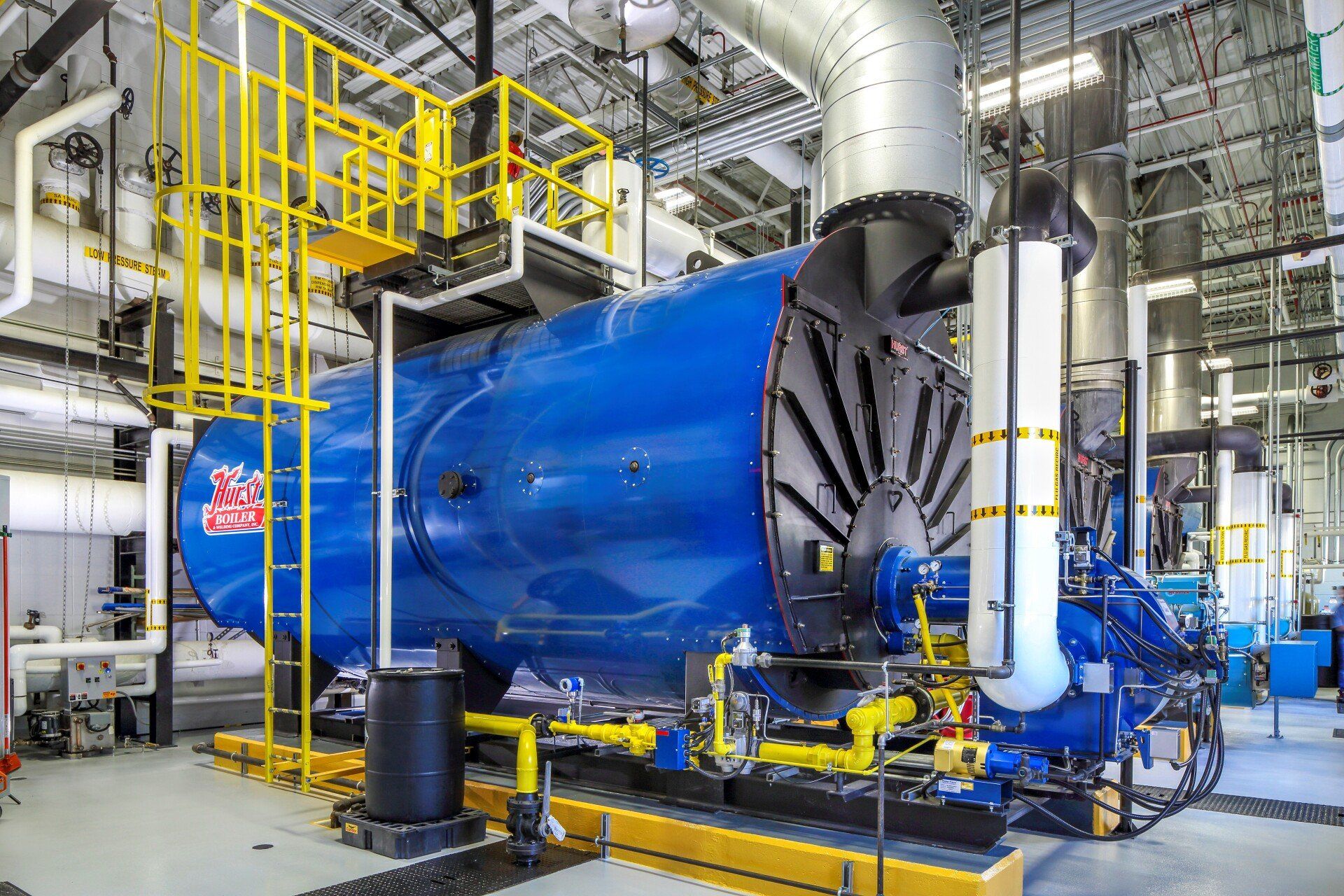 Blue industrial boiler in a utility room, with yellow access platforms and pipes.