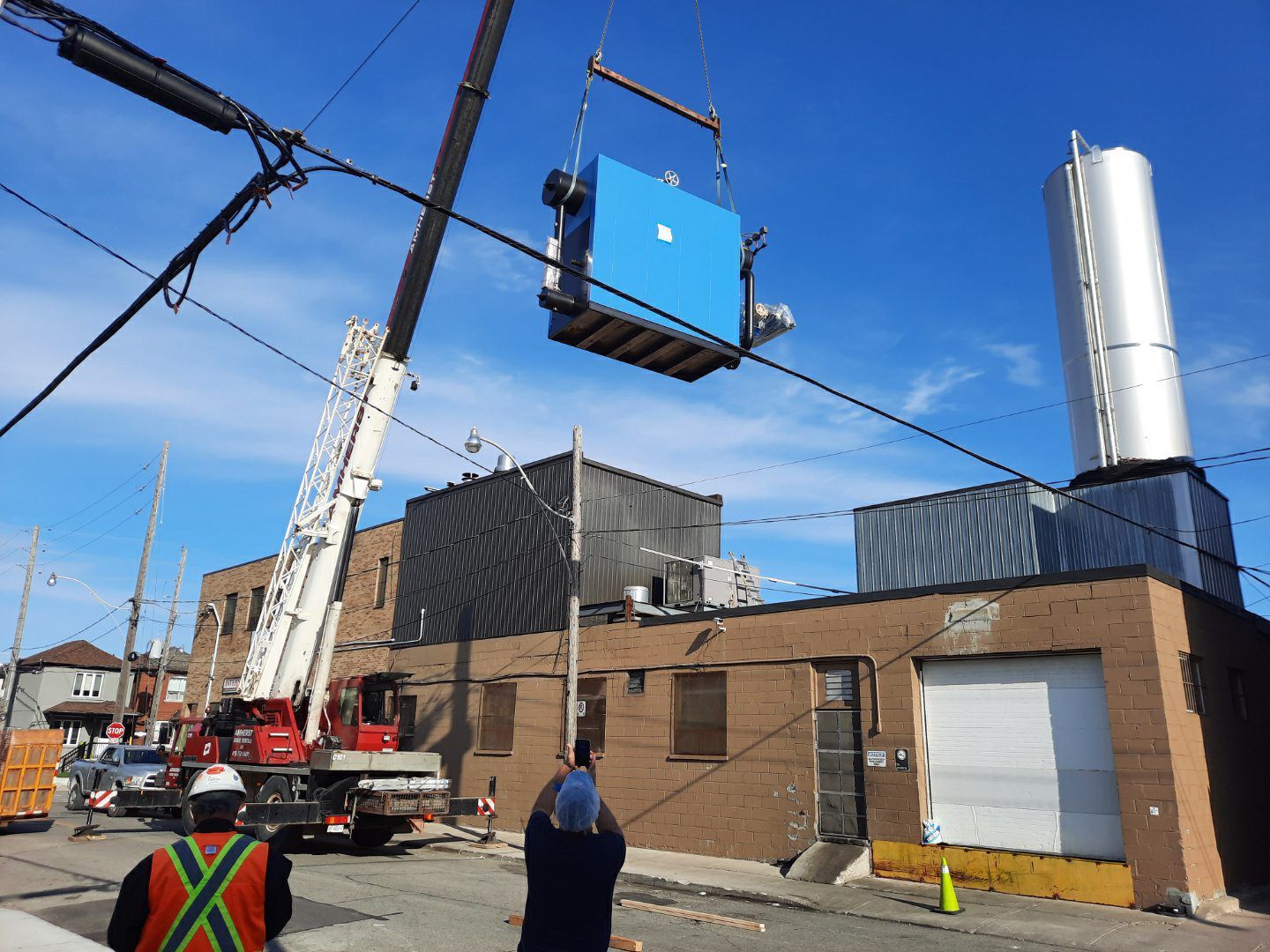 Crane lifting blue equipment box over industrial building.