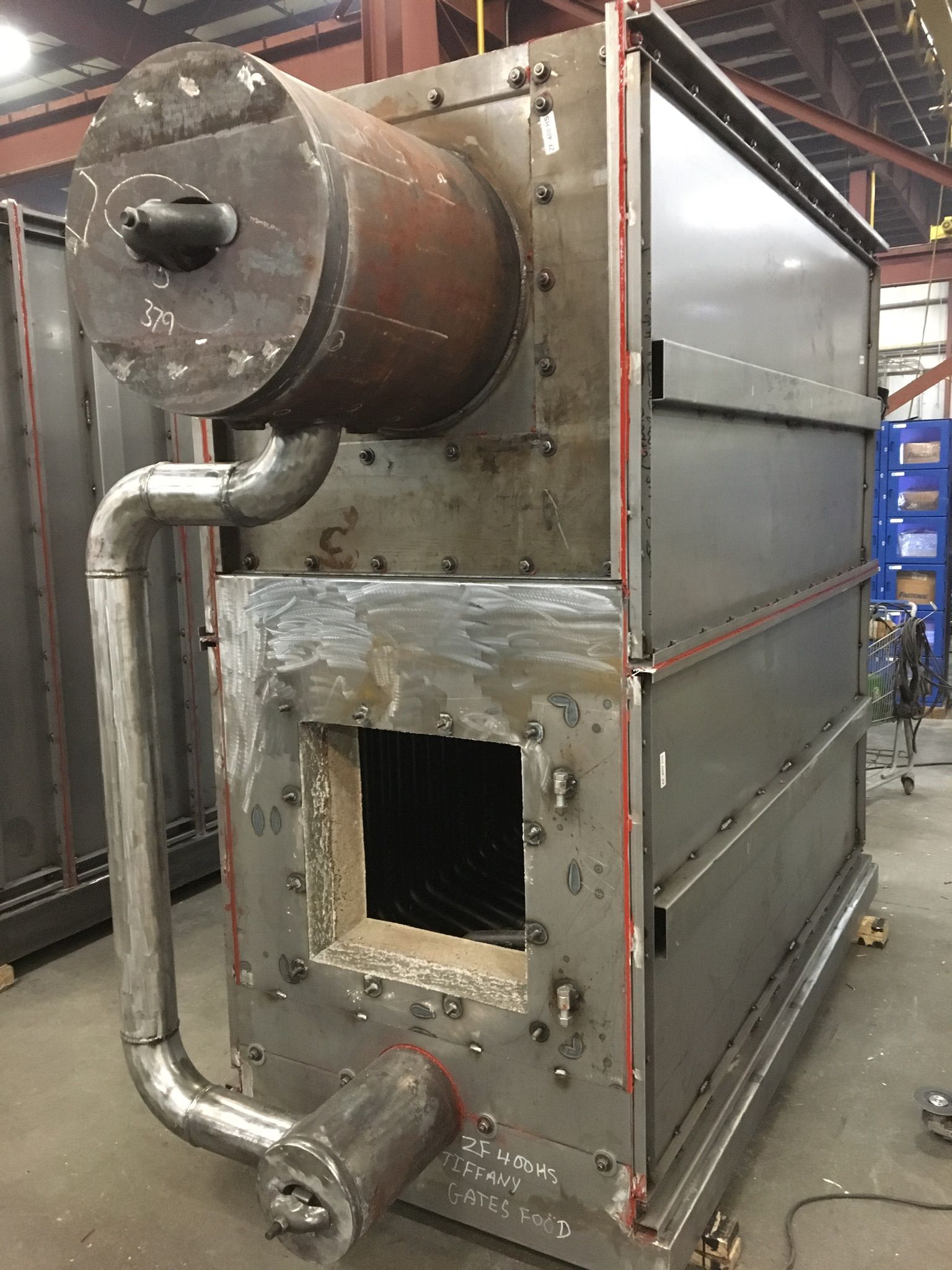 Large industrial metal furnace with a cylindrical combustion chamber, pipes, and a rectangular opening.
