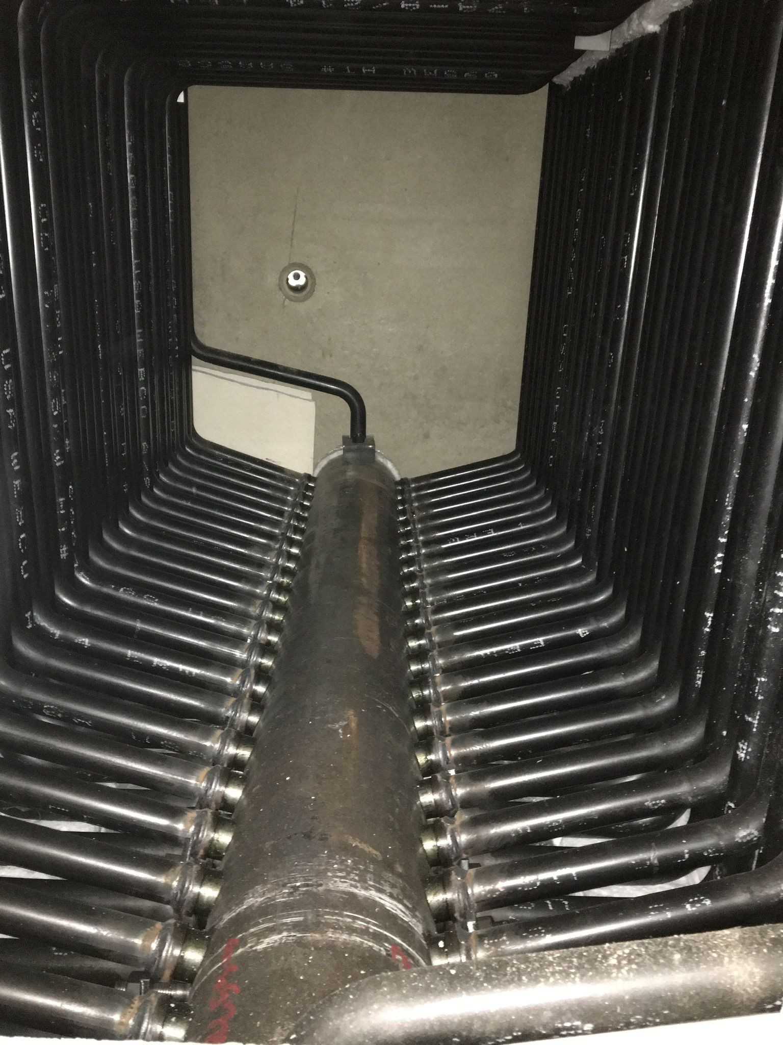 Black pipes in a rectangular configuration inside a utility room, possibly a heating system component.