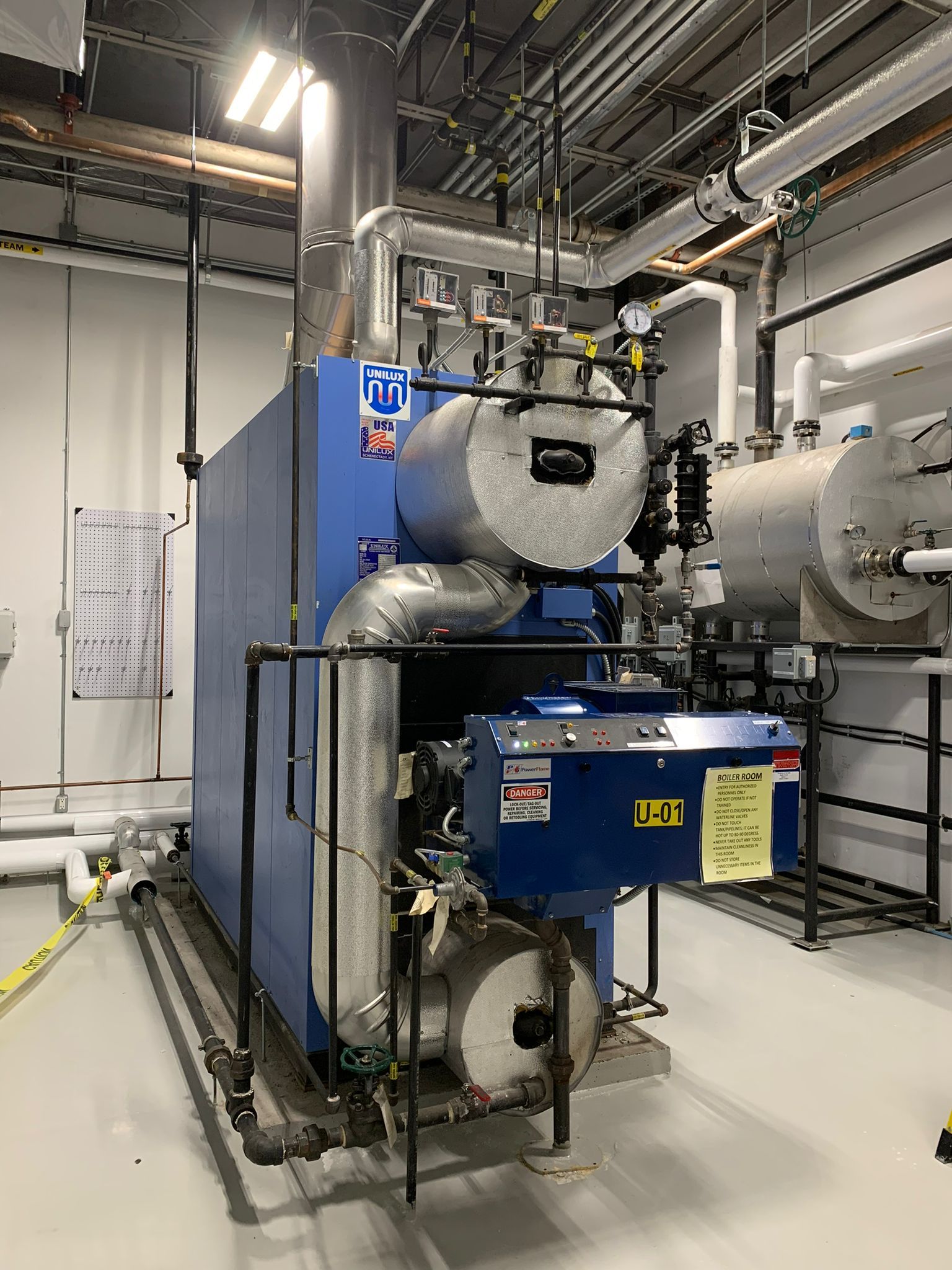 Blue industrial boiler in a clean room with piping and ventilation.