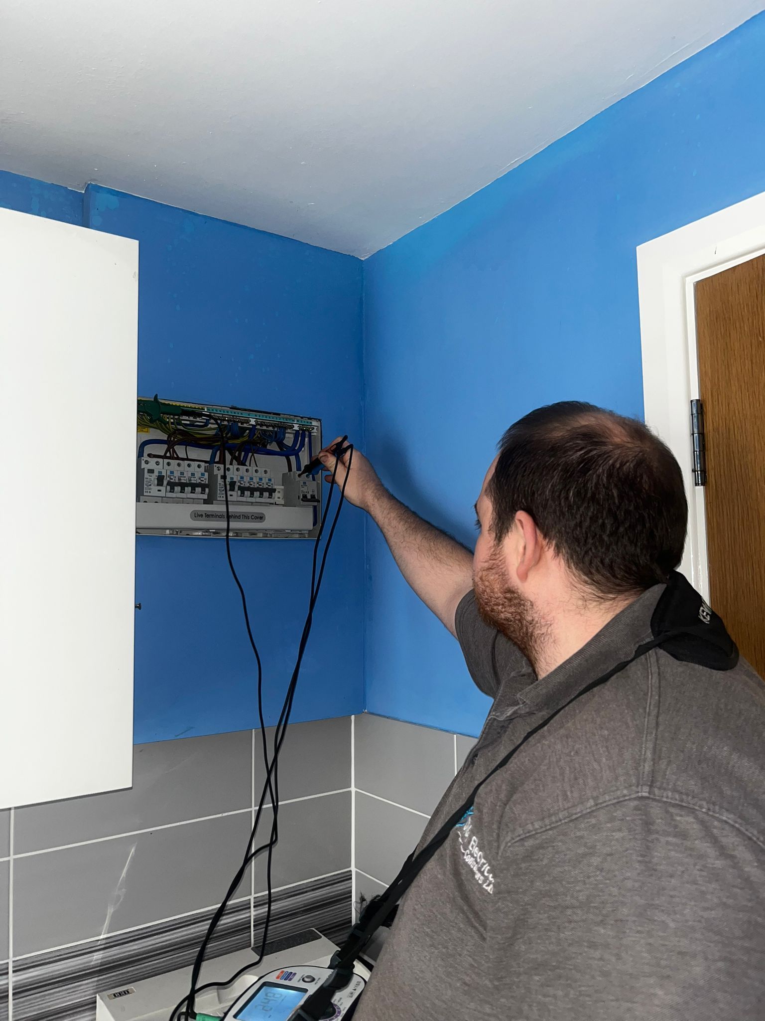 Technician adjusting equipment on a wall shelf in a blue room with cables hanging down.