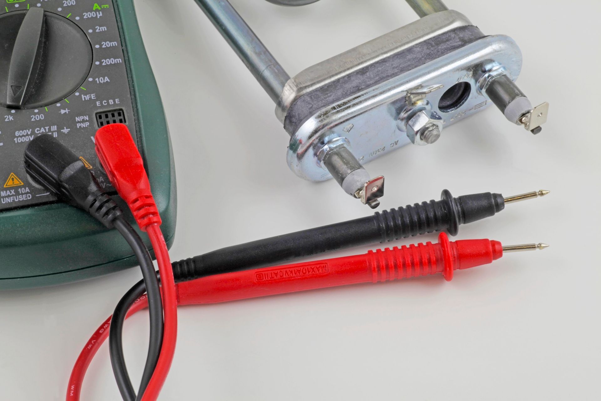 Multimeter with red/black leads testing a silver appliance heating element on a white surface.