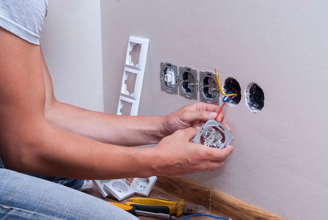 Person installing electrical outlet wires in a wall.