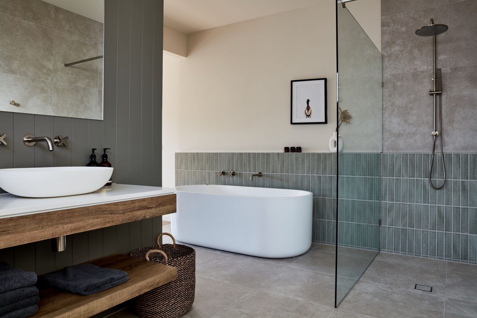 Modern bathroom with a white tub, shower, sink, and wooden shelves. Grey and neutral tones.