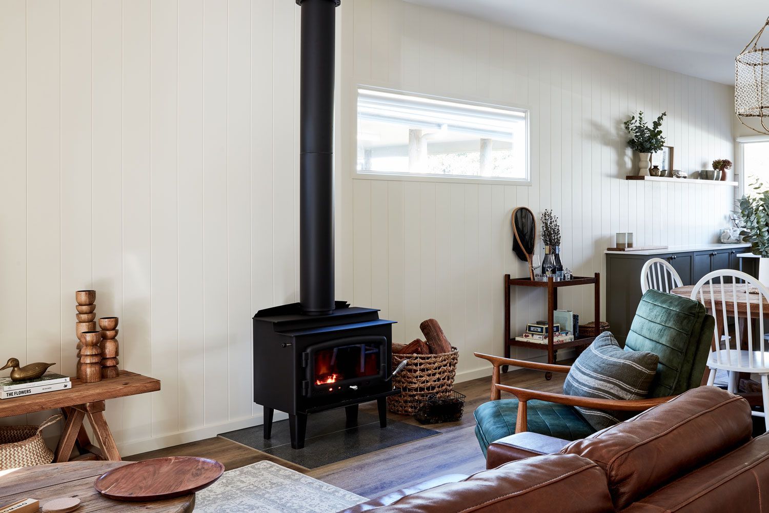 Living room with black wood-burning stove and chimney. Light walls, wood furniture, and a green armchair are present.