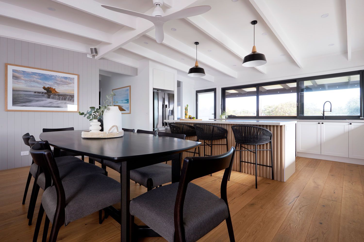 Dining room with a table, chairs, kitchen island, and ceiling beams.