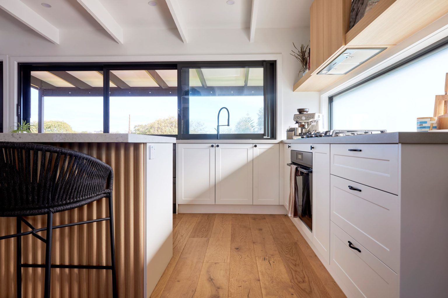 Modern kitchen with white cabinets, wood floors, and corrugated metal island.