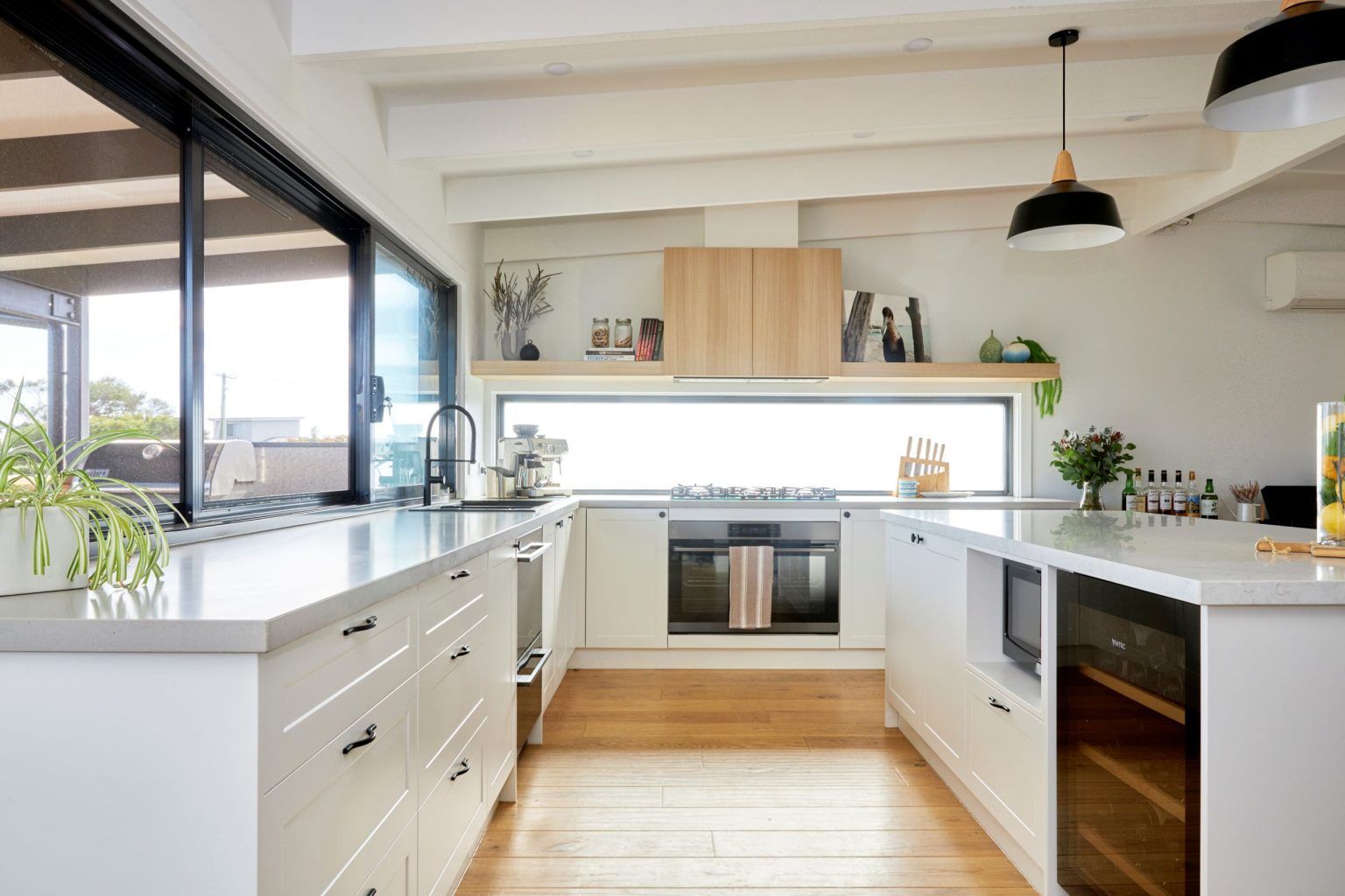 Modern kitchen with white cabinets, light wood floor, and large windows.