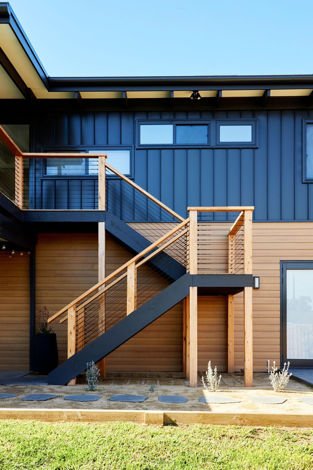 Exterior view of a modern house with a wooden deck and staircase, blue siding, and clear sky.