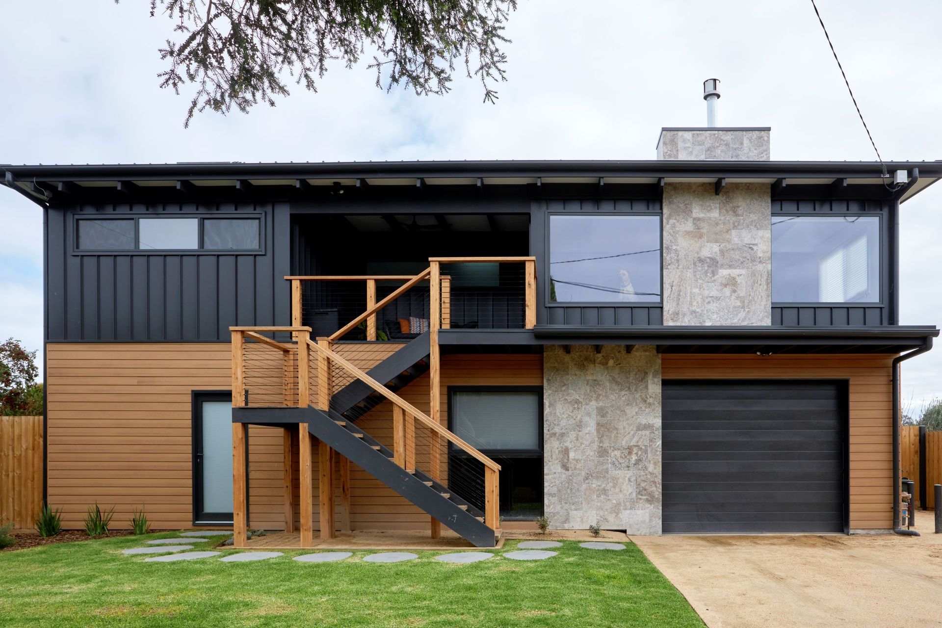 Two-story modern home with wood and black siding, stone accents, and an outdoor staircase.