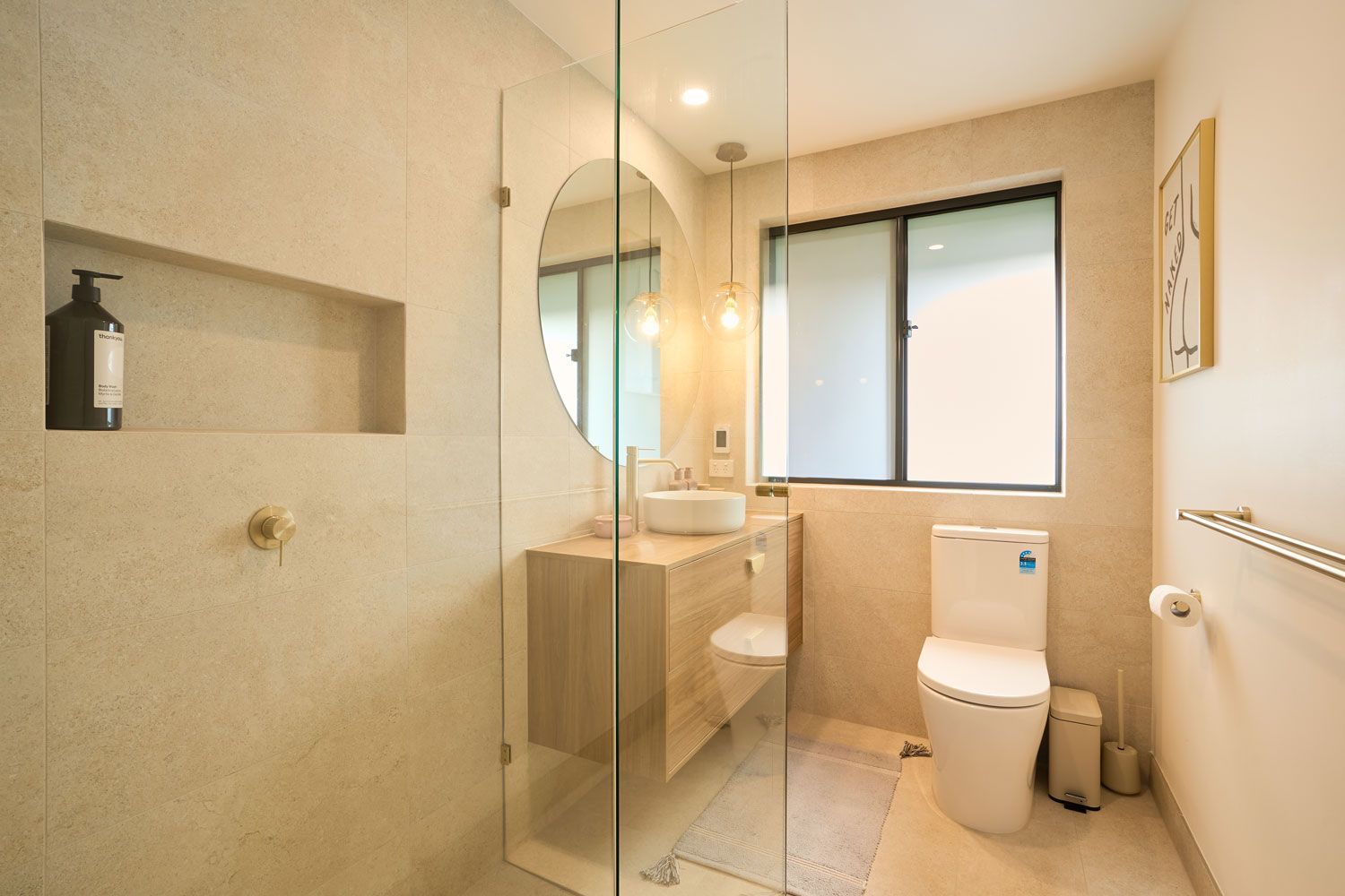 Modern bathroom with beige tile, glass shower, wooden vanity, and a toilet.