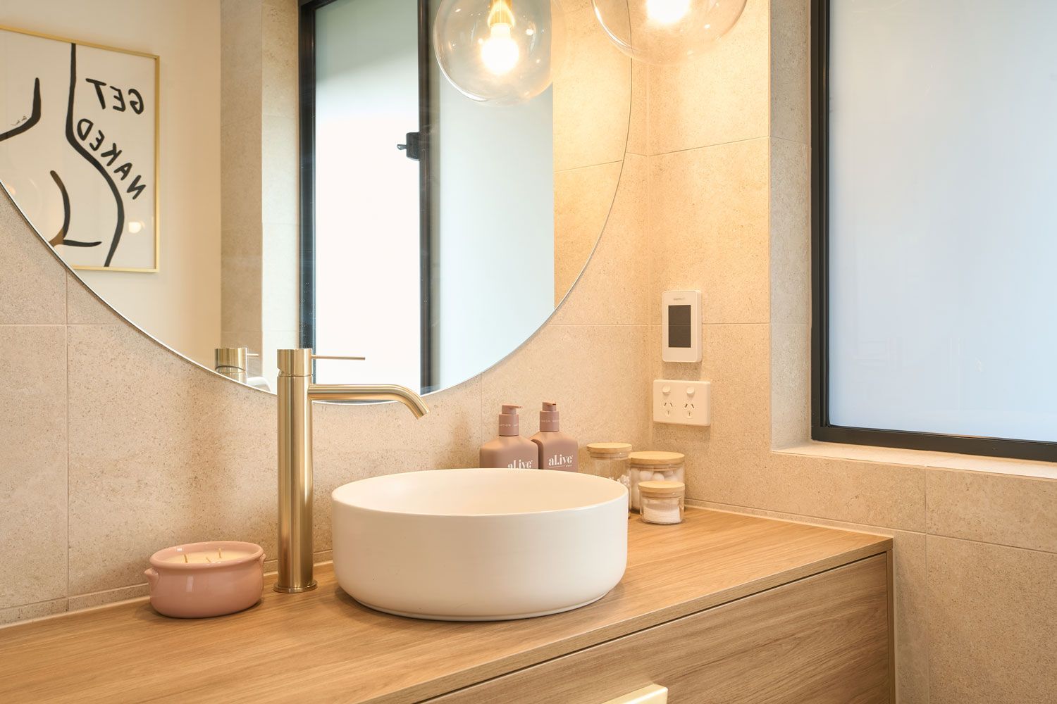 Bathroom sink with gold faucet, round mirror, and framed art; warm tones.