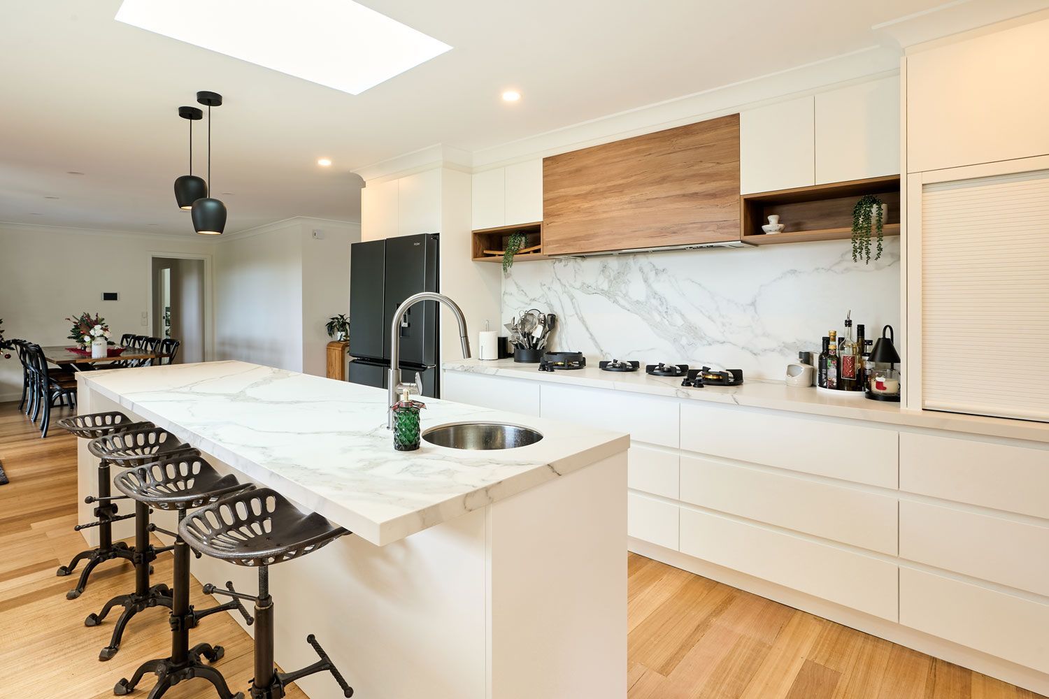 Modern kitchen with white cabinets, marble countertops, wooden accents, and a large island with seating.