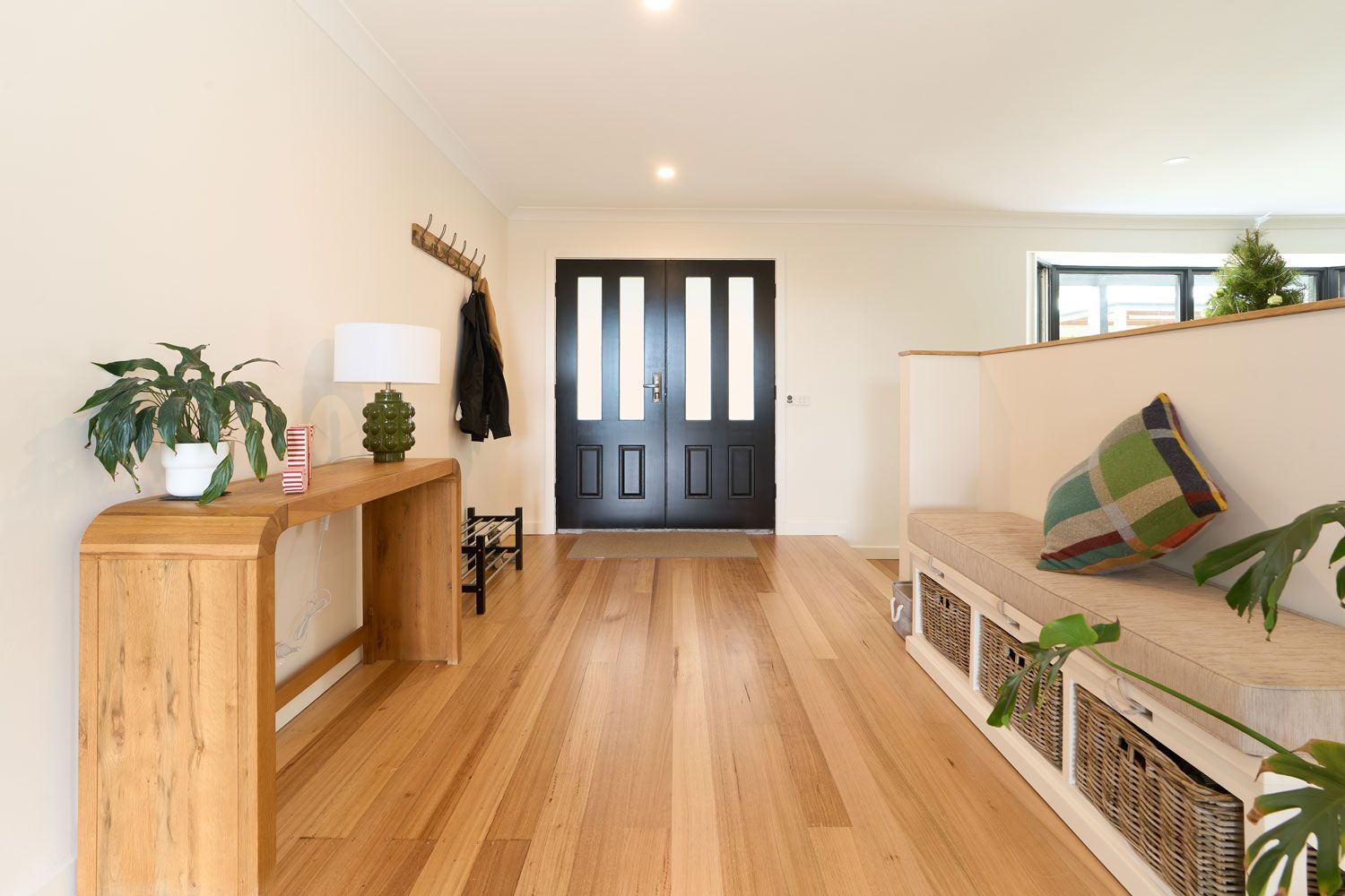 Hallway with wooden floor, black double doors, wooden console table with plants, and a bench with cushions.