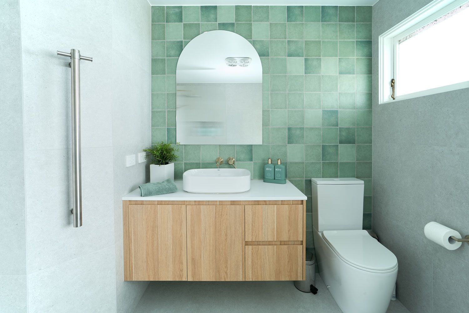 Bathroom with green tile accent wall, wooden vanity, and arched mirror.
