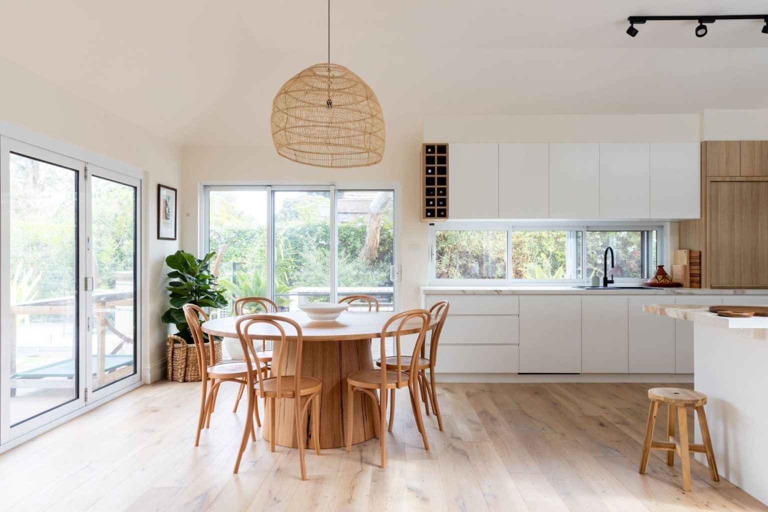 Dining room with a wooden table, chairs, white cabinets, and large windows.