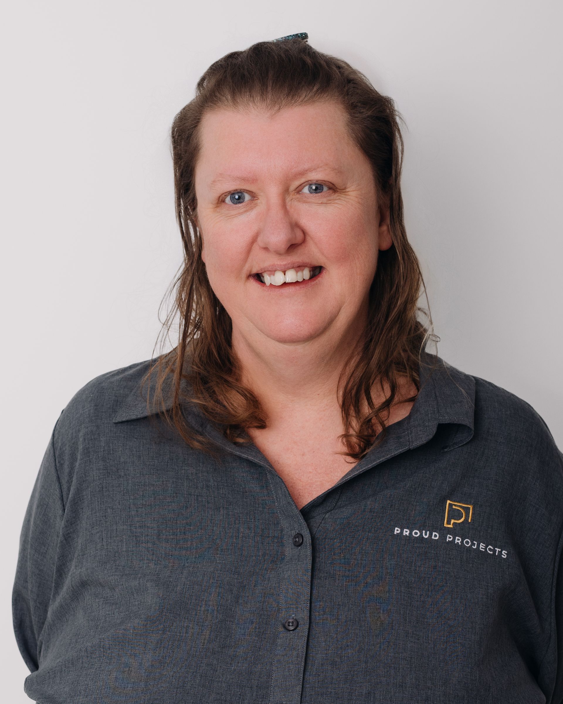 Woman in gray shirt smiles, facing the camera. Light background.