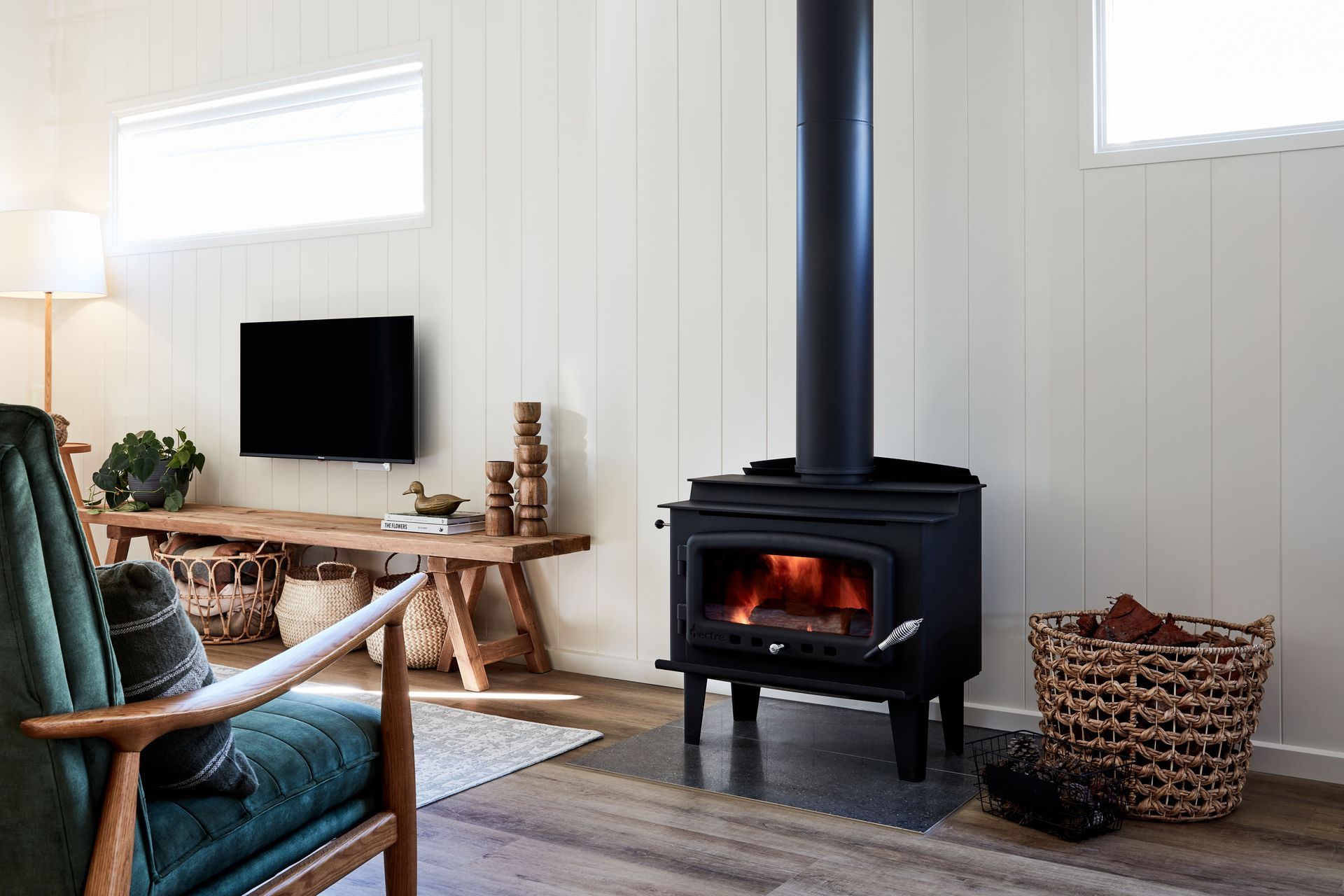 Cozy living room with a lit wood-burning stove. A TV, bench, and armchair are also present.