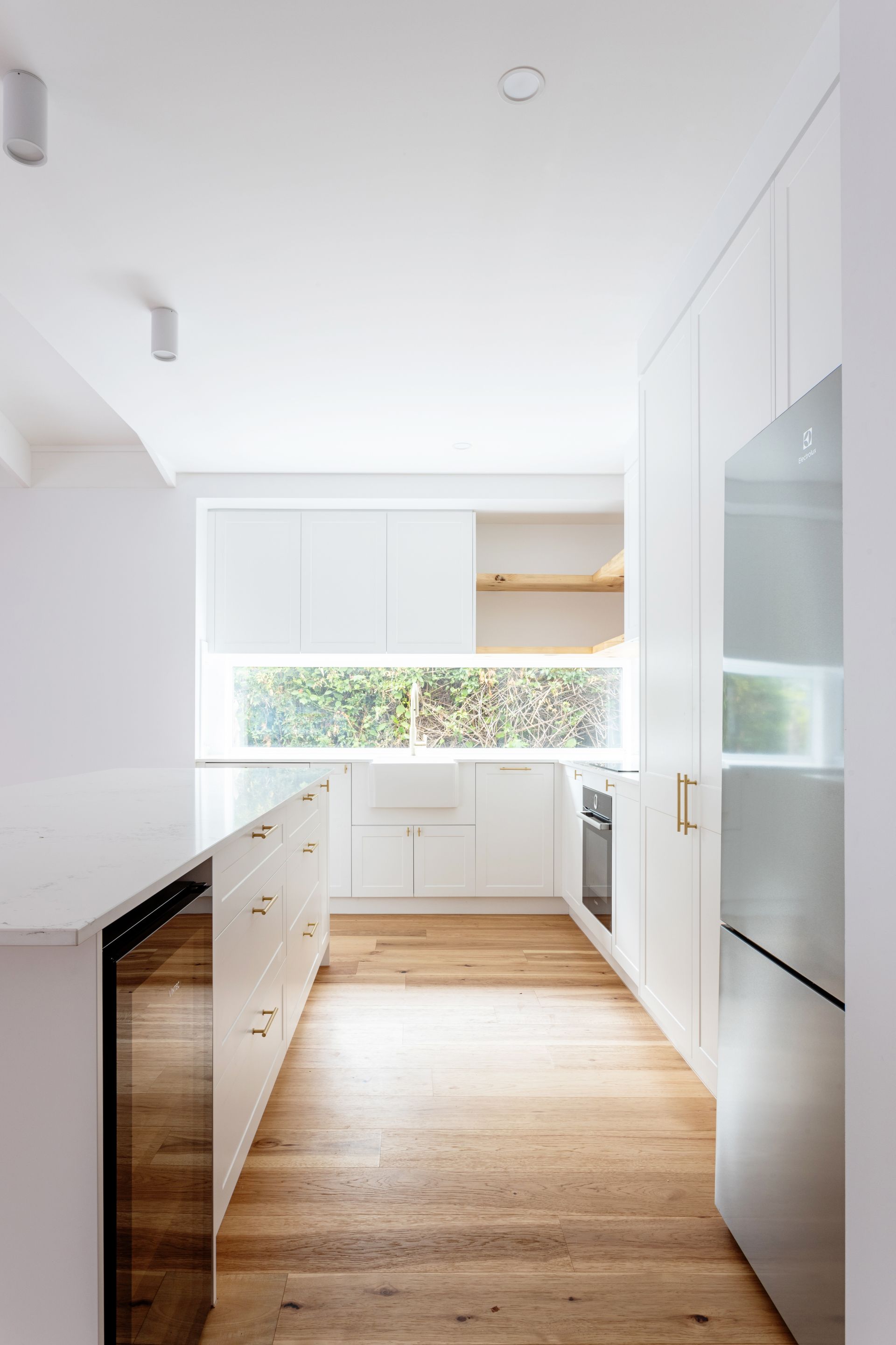 Bright white kitchen with light wood floors and large window looking out to greenery.