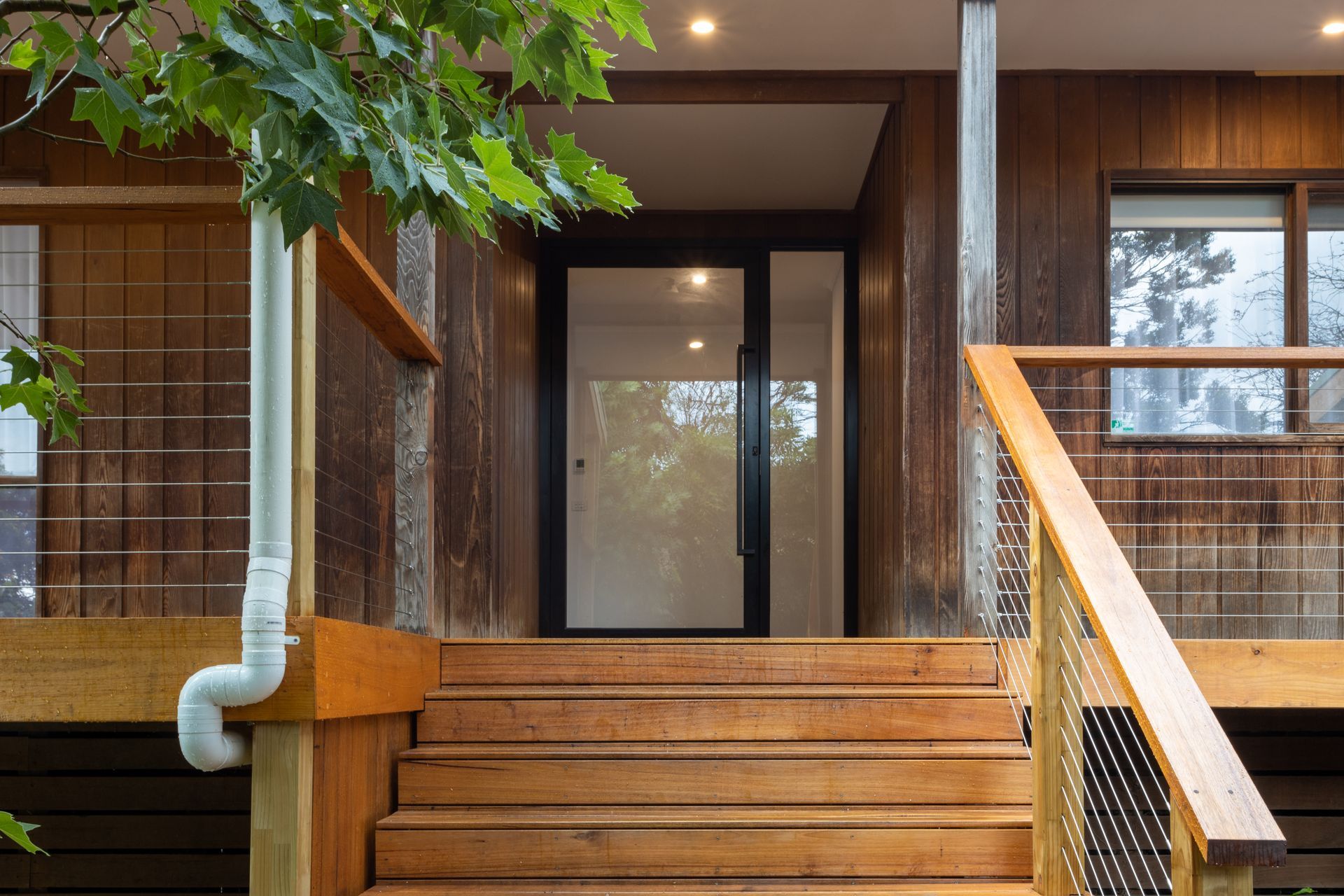 Wooden steps lead to a front door with glass panels. A covered porch and wooden siding are visible.