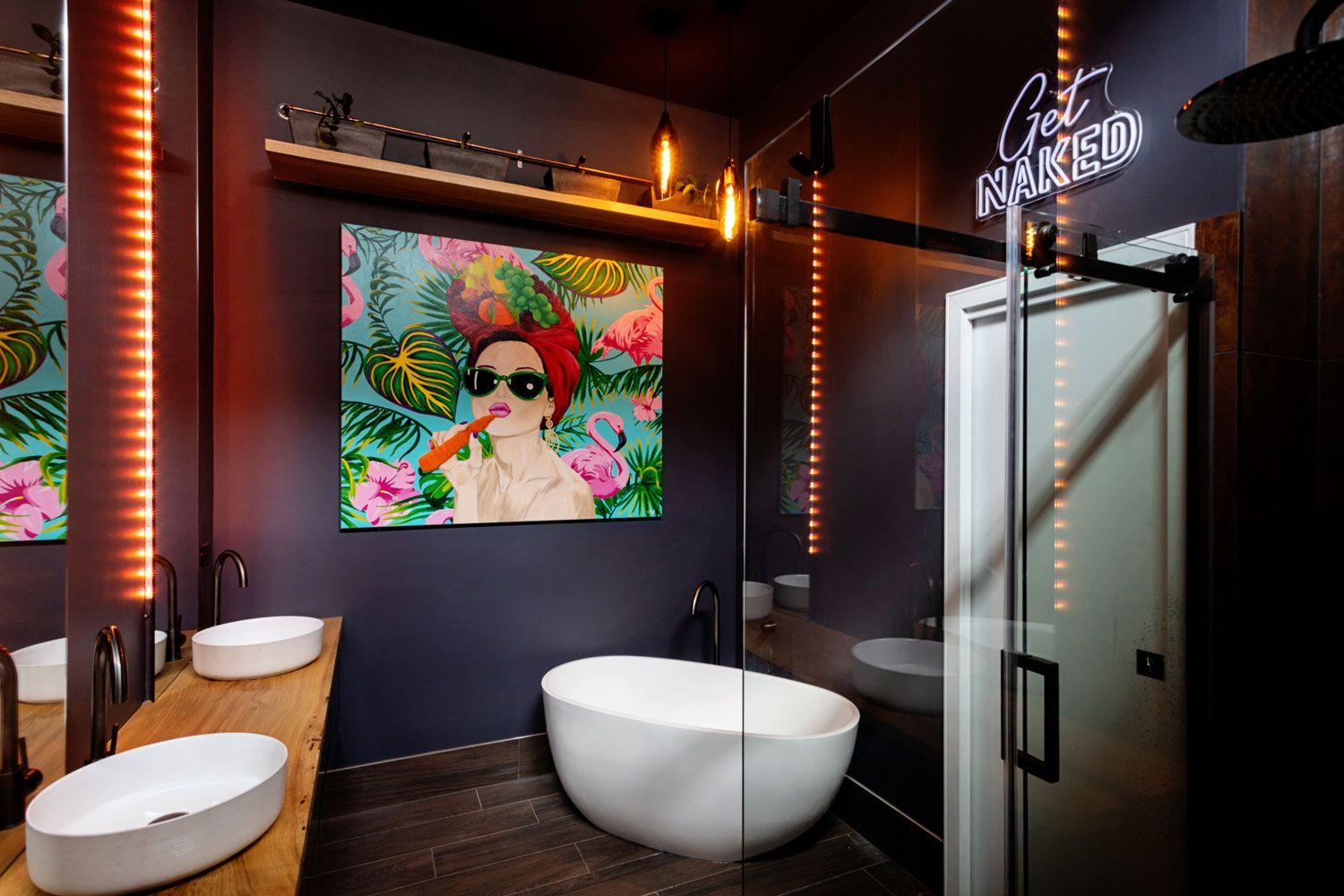 Modern bathroom with dark walls, white sinks, a bathtub, and tropical art.