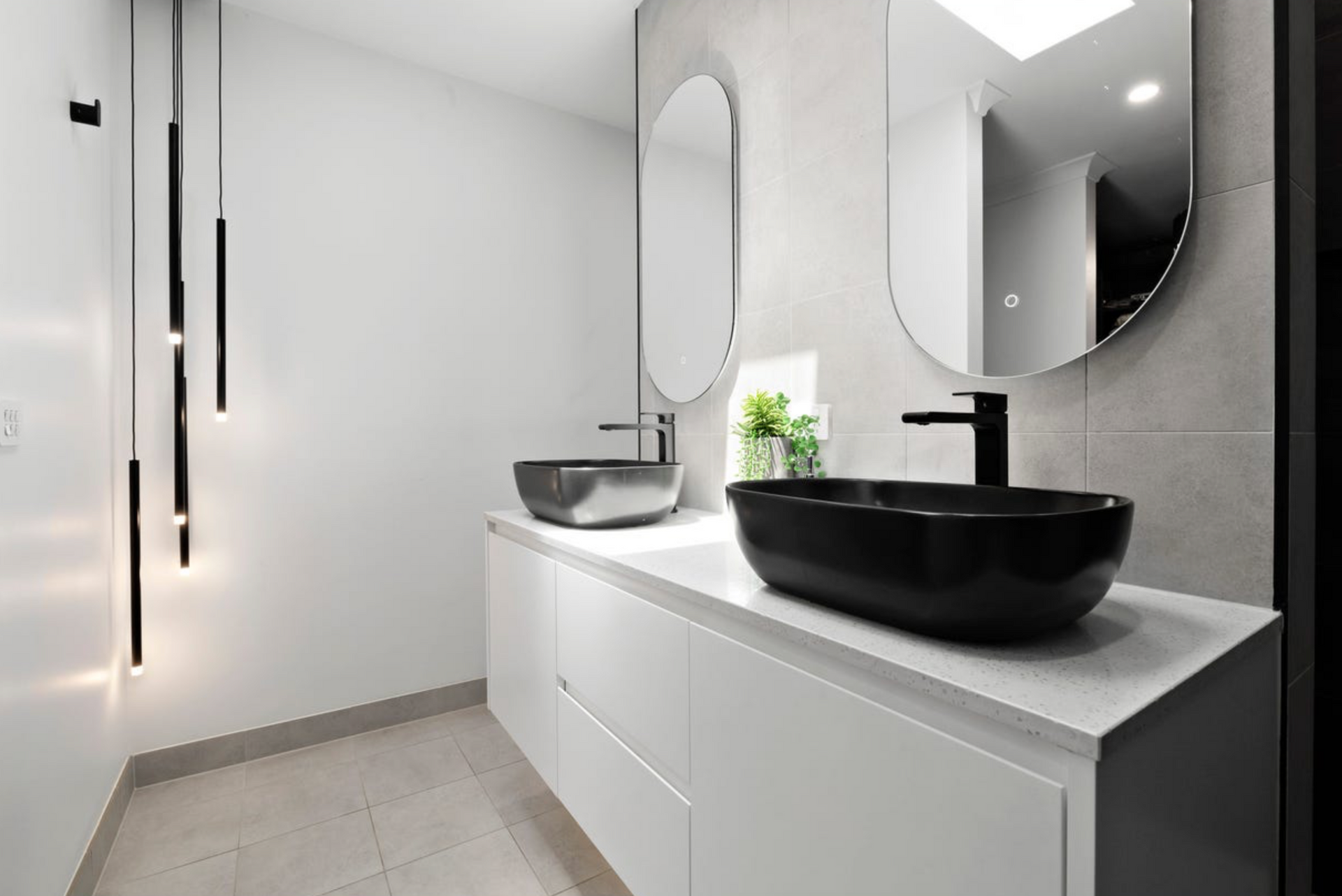 Modern bathroom with two sinks, oval mirrors, black fixtures, and white cabinetry.