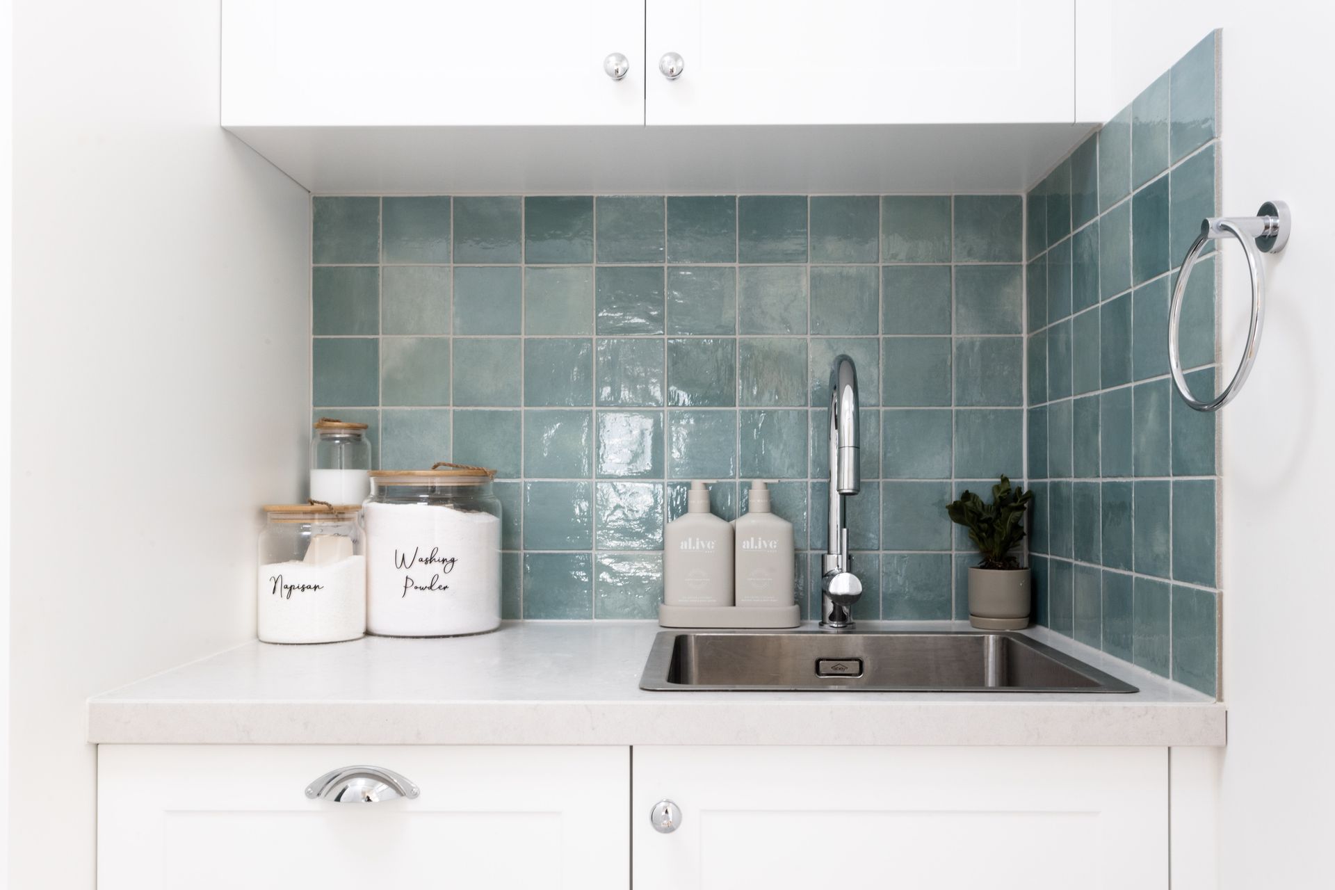 Laundry room with teal backsplash, white cabinets, and a stainless steel sink.
