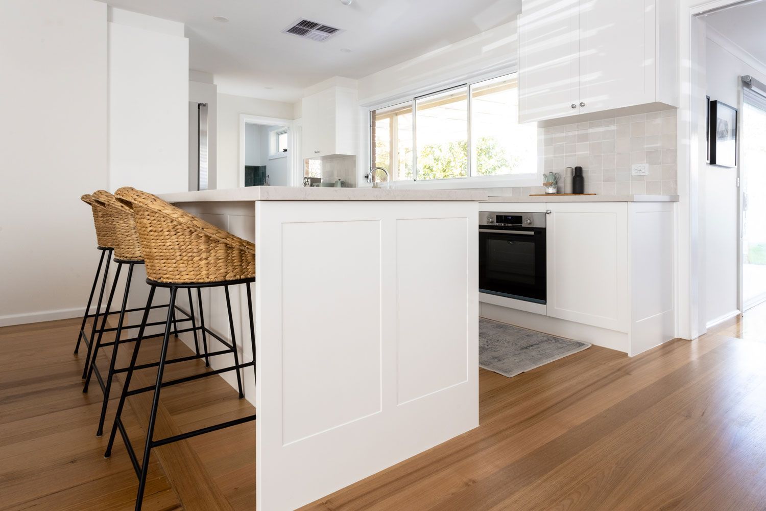 Modern white kitchen with island, bar stools, oven, and hardwood floors.
