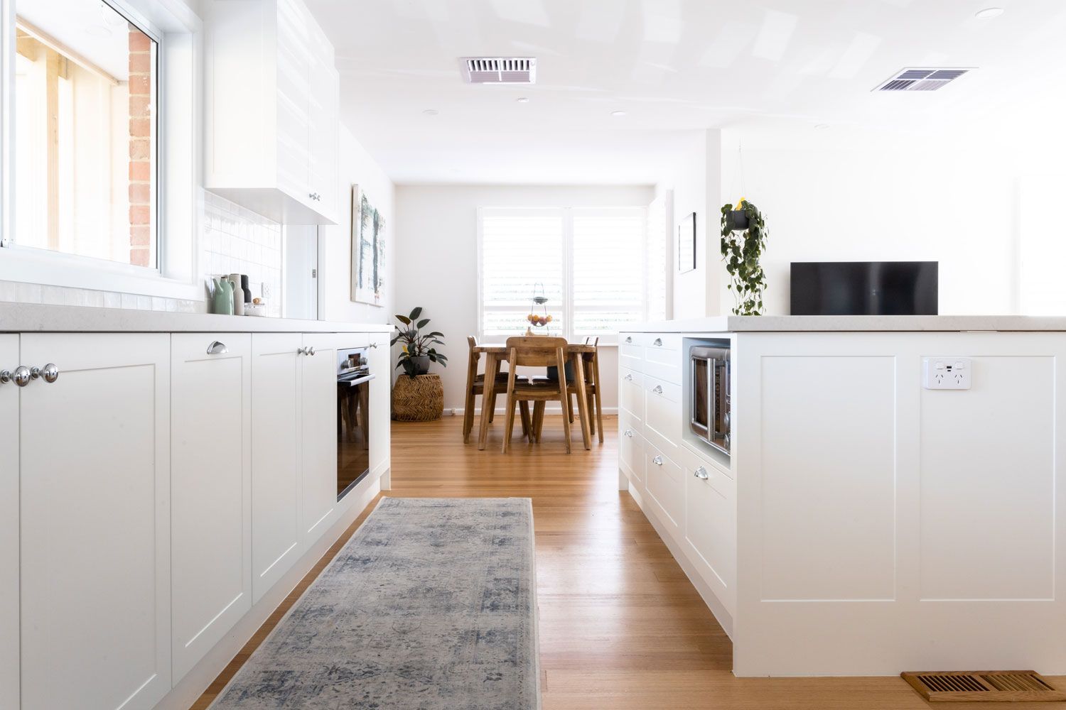 White kitchen with island, wooden floors, and dining table visible in the background.