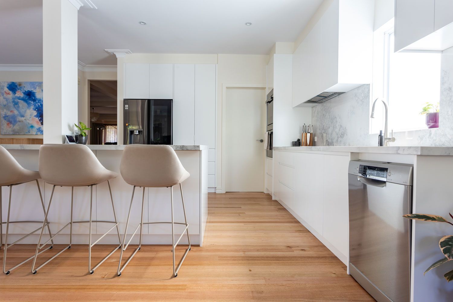 Modern white kitchen with wood floors, stainless steel appliances, and bar stools.