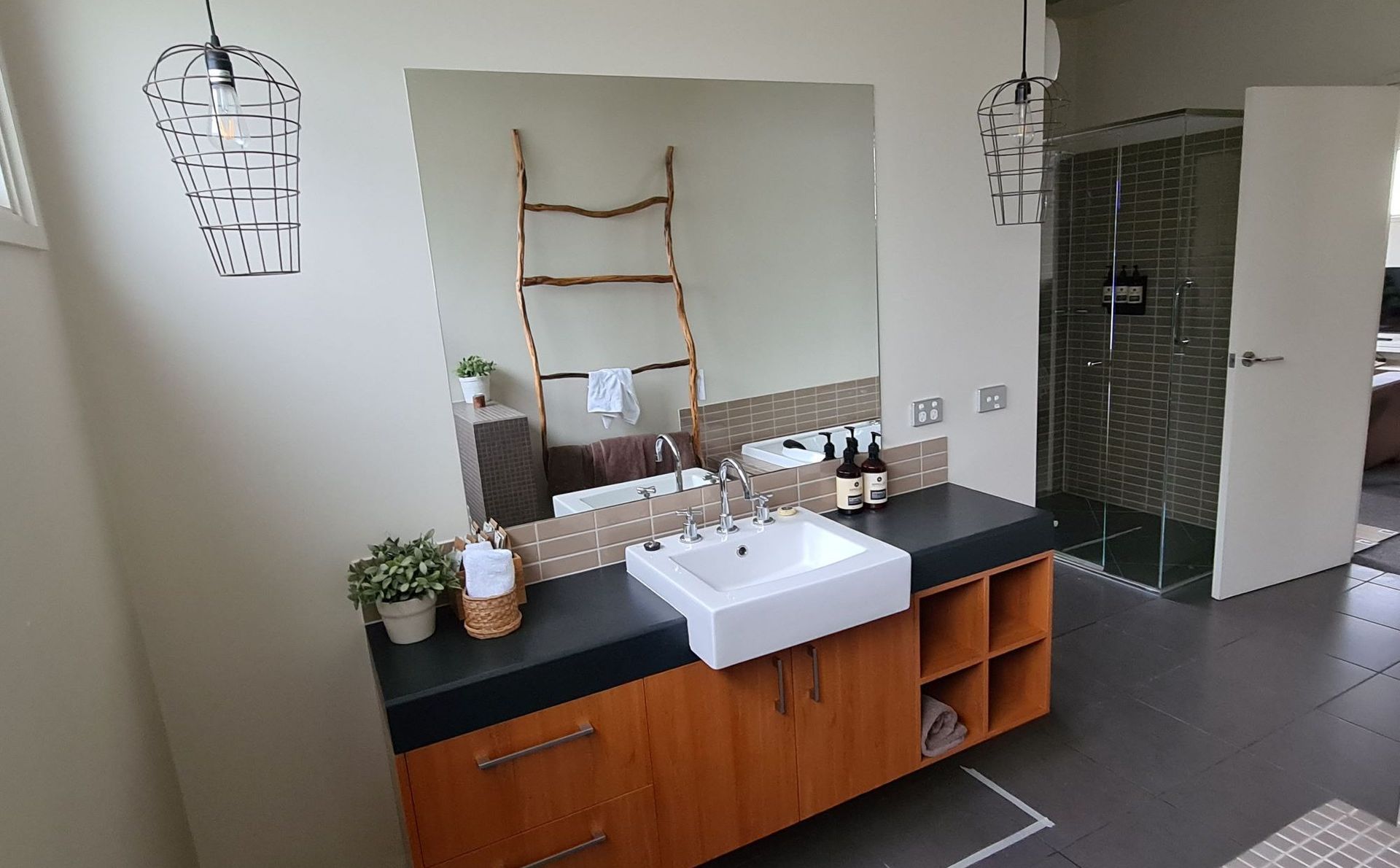 Bathroom with wooden vanity, white sink, and large mirror. Shower with dark tile.