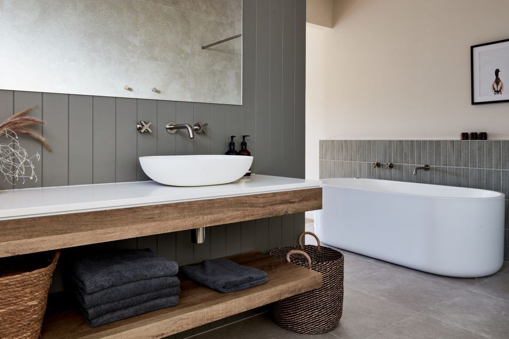 Modern bathroom with white tub, sink, and wooden vanity; gray wall panels and concrete floor.