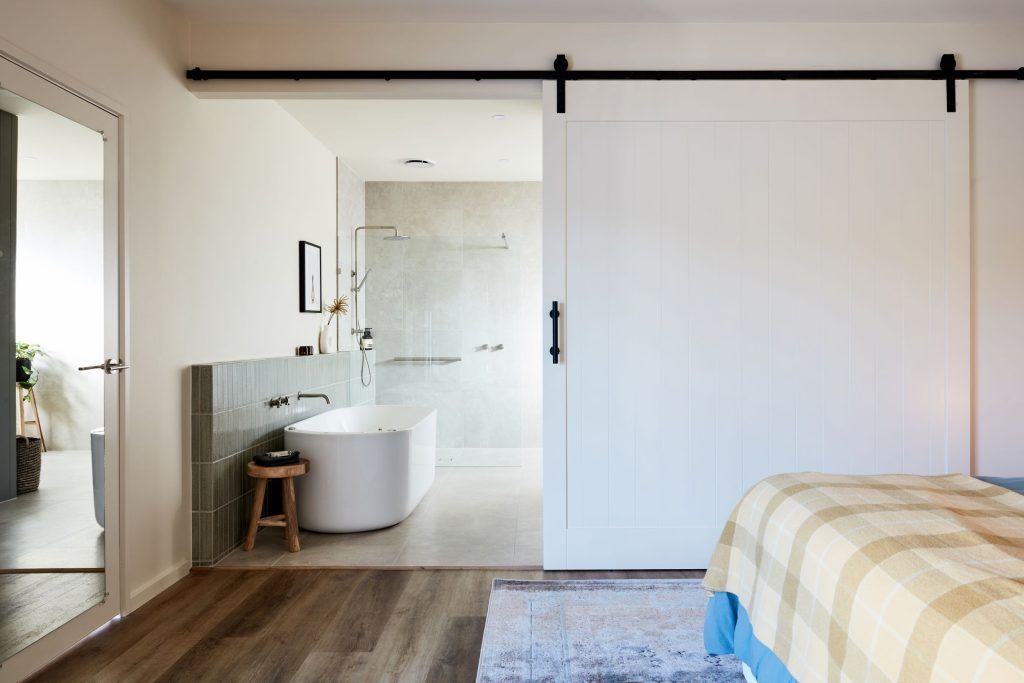 Bedroom with sliding white barn door revealing a modern bathroom with a bathtub.