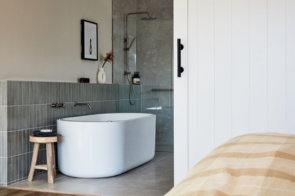 Modern bathroom with a white bathtub, gray tile, and wooden stool.