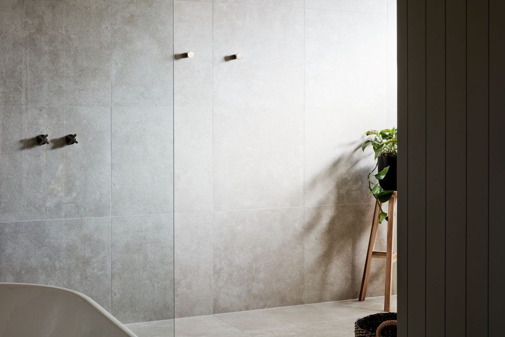 Bathroom with gray stone tile walls, modern fixtures, and a wooden ladder with plants.