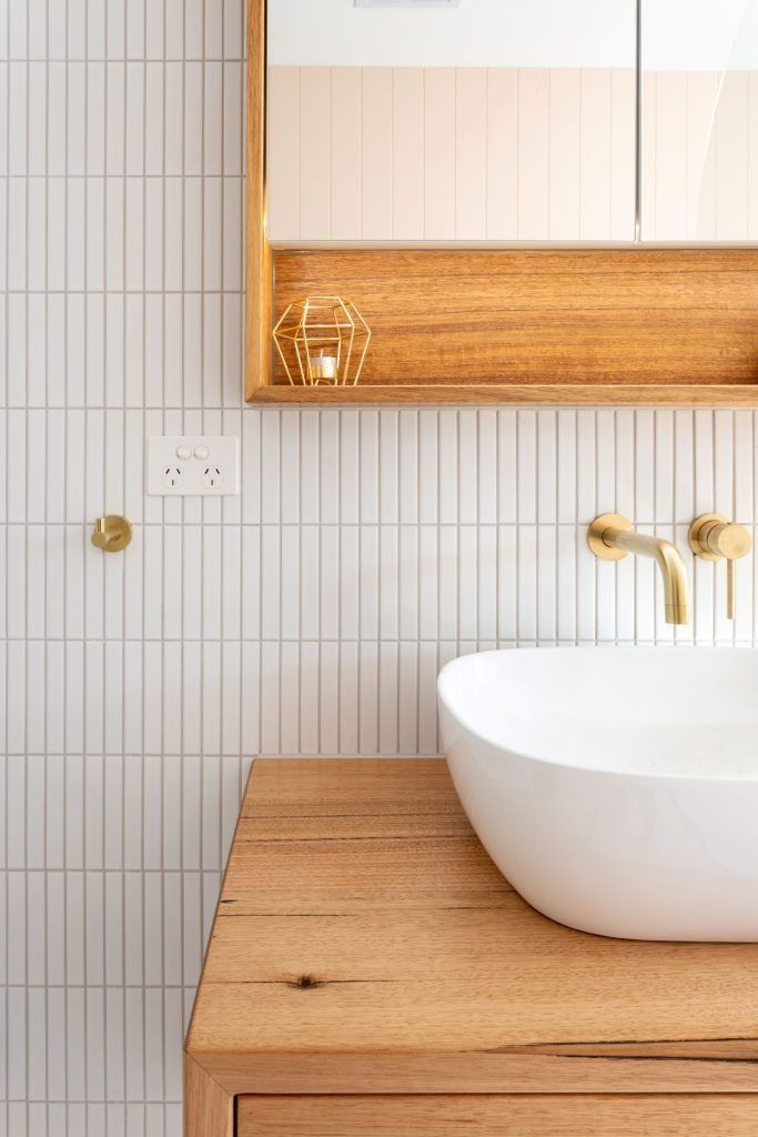 Bathroom with white vertical tile, wood vanity, and gold fixtures. White sink and cabinet.