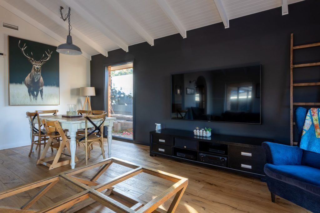 Living room with a dark accent wall, TV, dining table, and blue armchair.