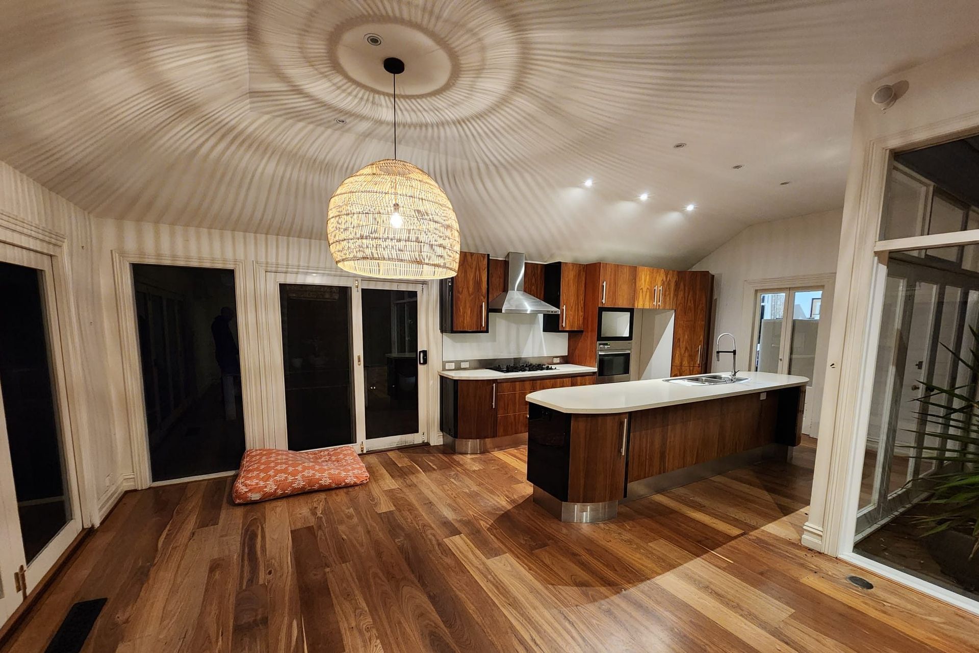 Spacious kitchen with wood cabinets and flooring, island, and large woven pendant light.