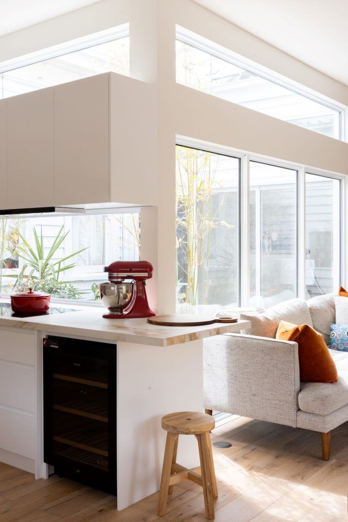 Modern kitchen with white cabinets, red mixer, and a windowed living area with a sofa.