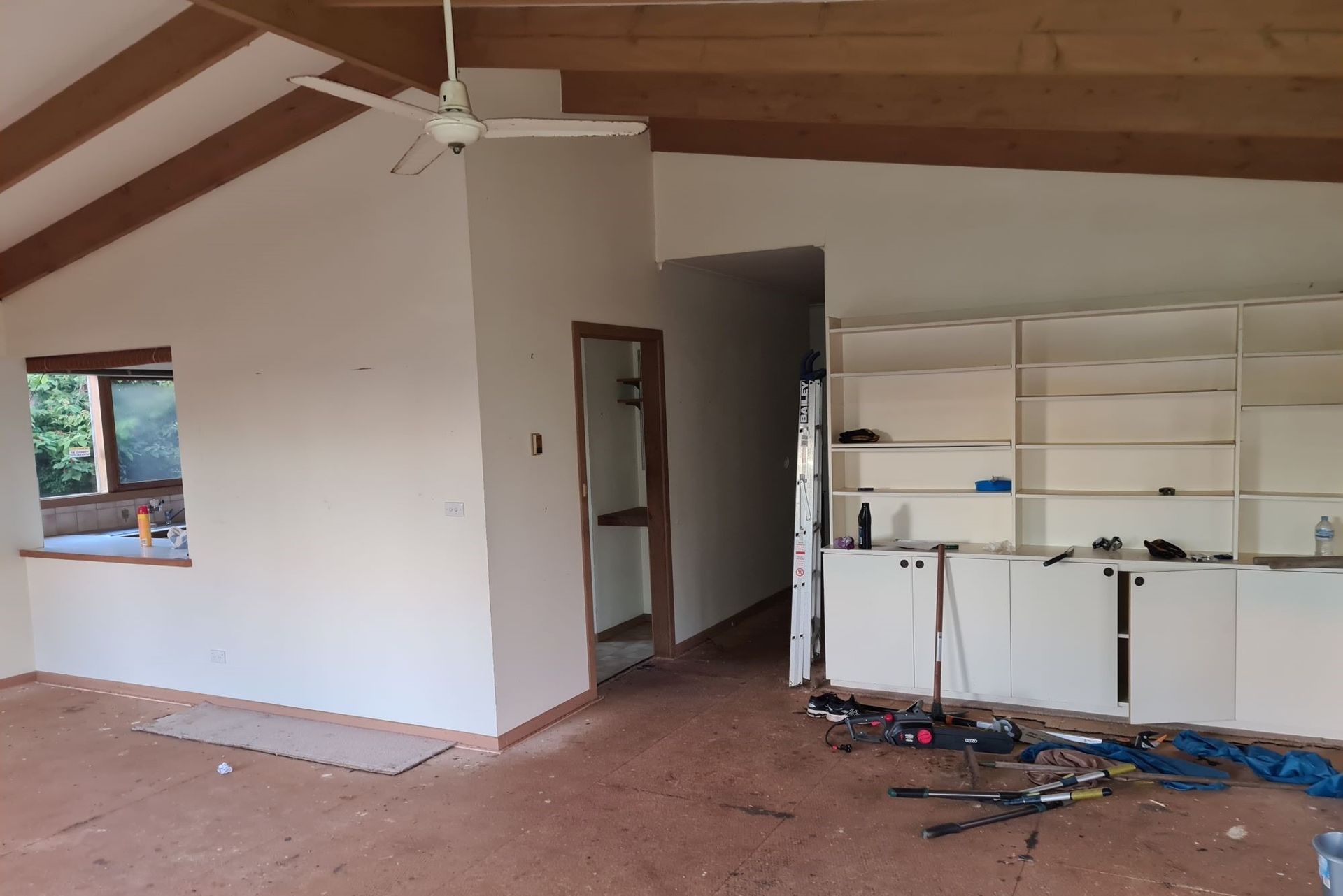 Interior view of a room under construction with white walls, wooden beams, and built-in white cabinets.