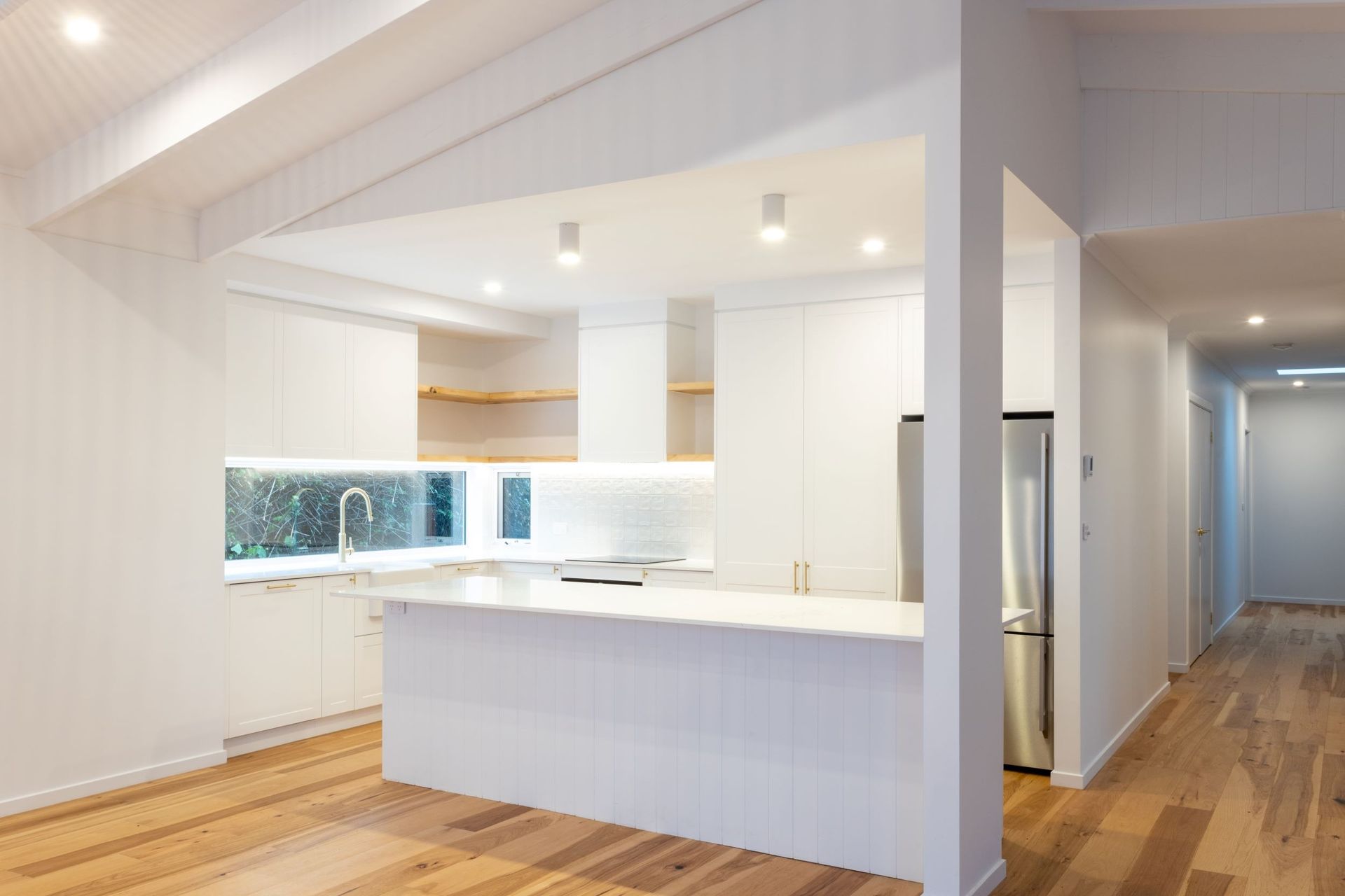 Modern white kitchen with island and stainless steel refrigerator. Wooden floors and exposed beams.